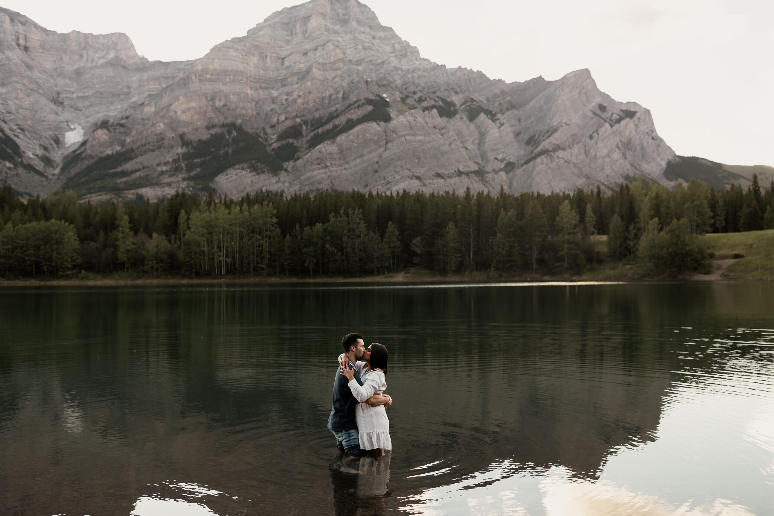 Couple share a kiss in the water at wedge pond in kananaskis